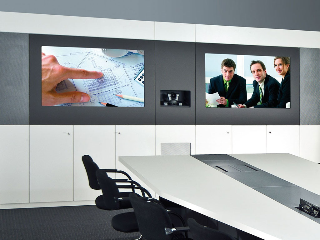Media wall with two screens, video conferencing module and cabinets in a meeting room with conference table